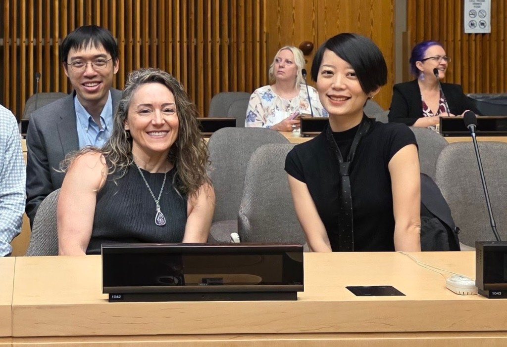Leah Wasser and Qianqian Ye smile at their seats in a UN conference chamber before co-leading an AI in open source session at the Maintain-a-Thon.