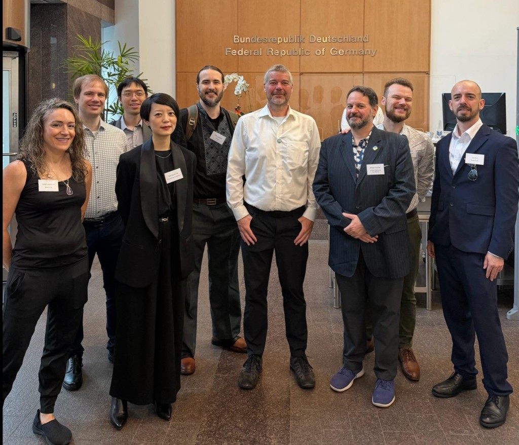 Open source maintainers and delegates pose together in the lobby of the German house in New York City during UN Open Source Week 2026, with Bundesrepublik Deutschland signage on the wall behind them.